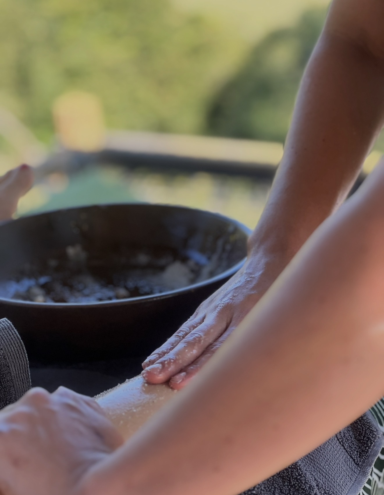 A therapist massaging a guest's arm with flowing oil strokes beside a black bowl of oil